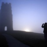 Турист делает фотографию башни Св. Михаила разрушенной церкви 14 века. Восходящее солнце начинает очищать землю от утреннего тумана.  4 сентября 2013 в Сомерсете, Англия.